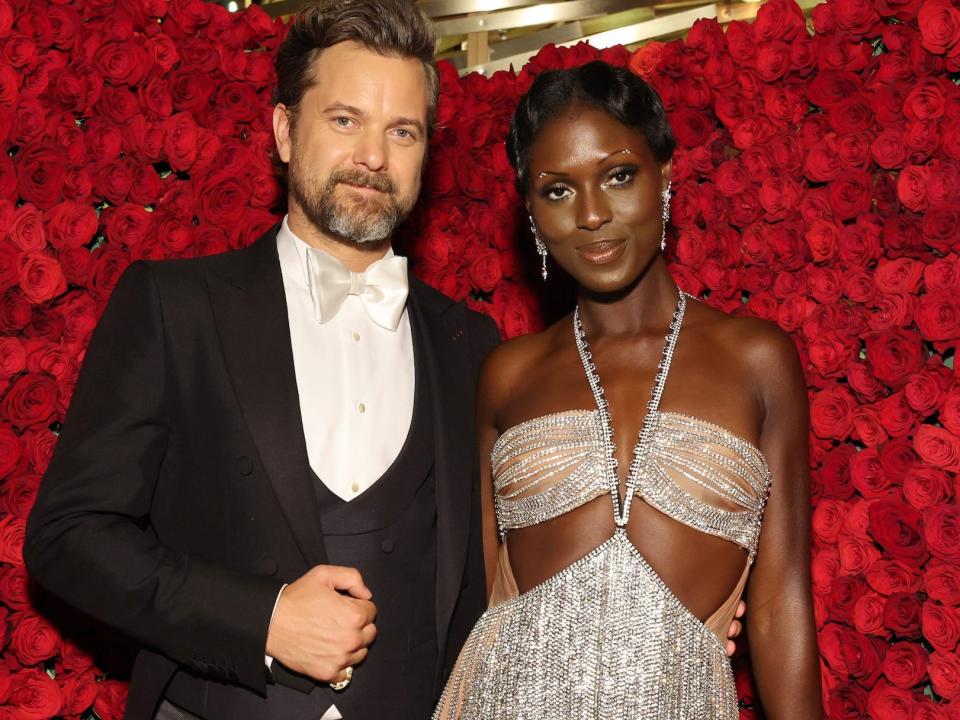 Joshua Jackson, in a black jacket with tails, and Jodie Turner-Smith, in a sparkly silver bodysuit, pose in front of a background of roses at the 2022 Met Gala.