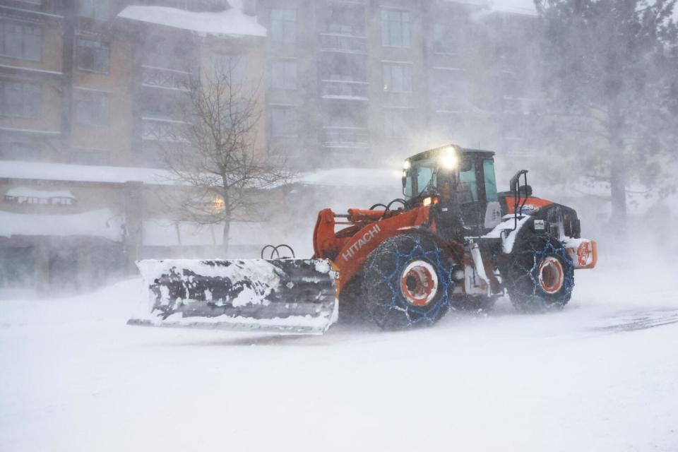 Heavy snow removal equipment rolls down a snowy street.