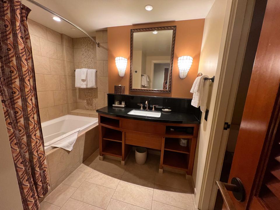 A hotel bathroom with a single sink, shower tub combo, and towels.