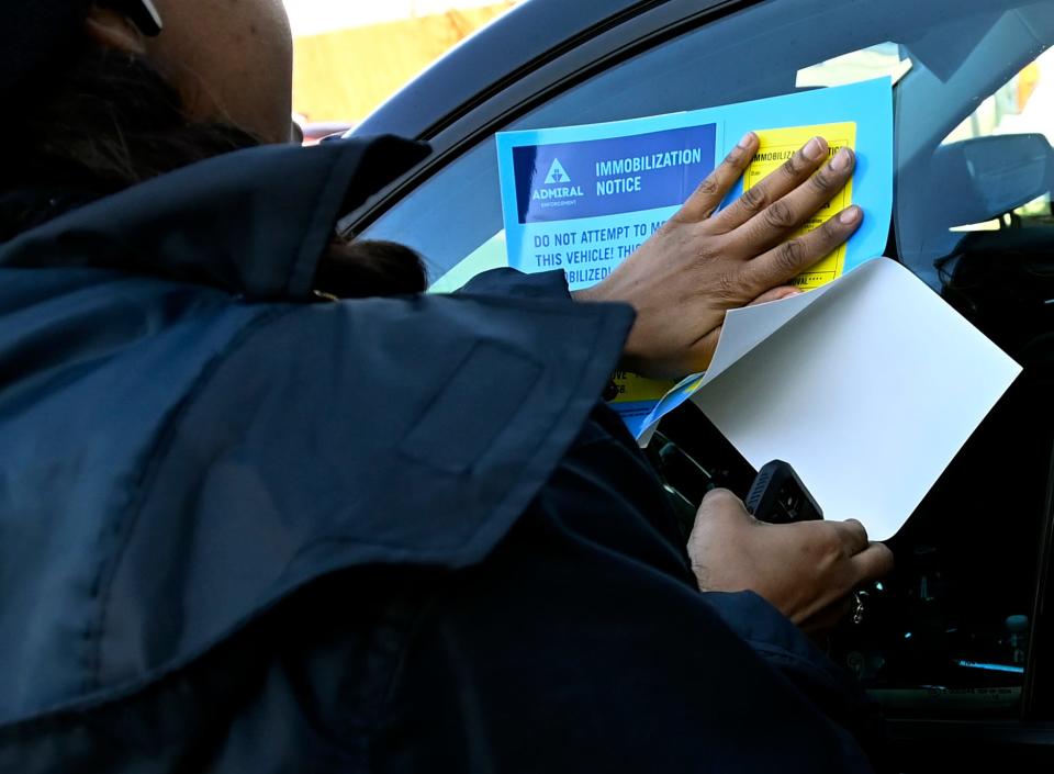 An employee of Admiral Parking Enforcement places a immobilization notice on a booted vehicle in a paid parking lot on Monday, Feb. 19, 2024, in Nashville, Tenn. Local and officials are working on stronger regulations for the companies that boot cars. Unlike some companies that provide no grace period, Admiral Parking gives drivers 30 minutes to move their vehicles before attaching a boot to the back driver’s side wheel.