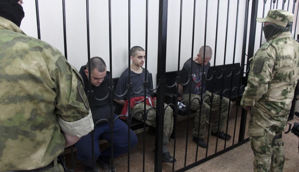 Two British citizens Aiden Aslin, left, and Shaun Pinner, right, and Moroccan Saaudun Brahim, center, sit behind bars in a courtroom in Donetsk, in the territory which is under the Government of the Donetsk People's Republic control, eastern Ukraine, Thursday, June 9, 2022. The two British citizens and a Moroccan have been sentenced to death by pro-Moscow rebels in eastern Ukraine for fighting on Ukraine's side. The three men fought alongside Ukrainian troops and surrendered to Russian forces weeks ago. (AP Photo)