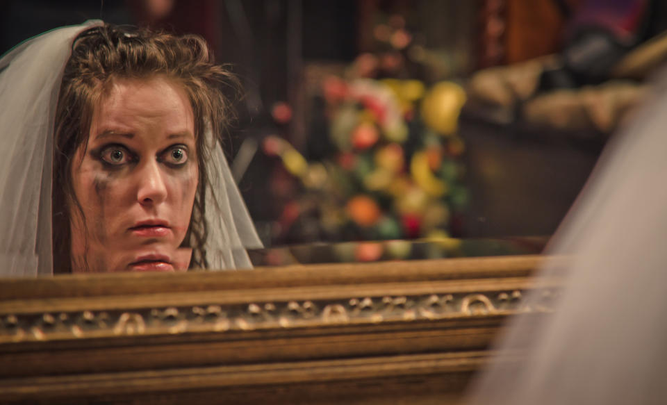 Bride in a distressed state with smeared makeup looks into a mirror anxiously. She has a veil and appears worried on her wedding day