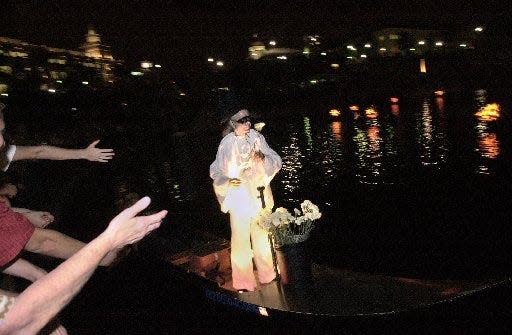 Mime Michael Grando rides in the bow of a boat through the water of Waterplace Park handing out flowers to the crowds that line the banks of the park.