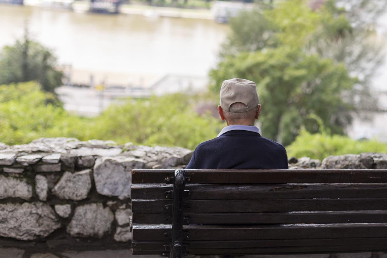 lonely old man sitting on a bench in a park, looking at river