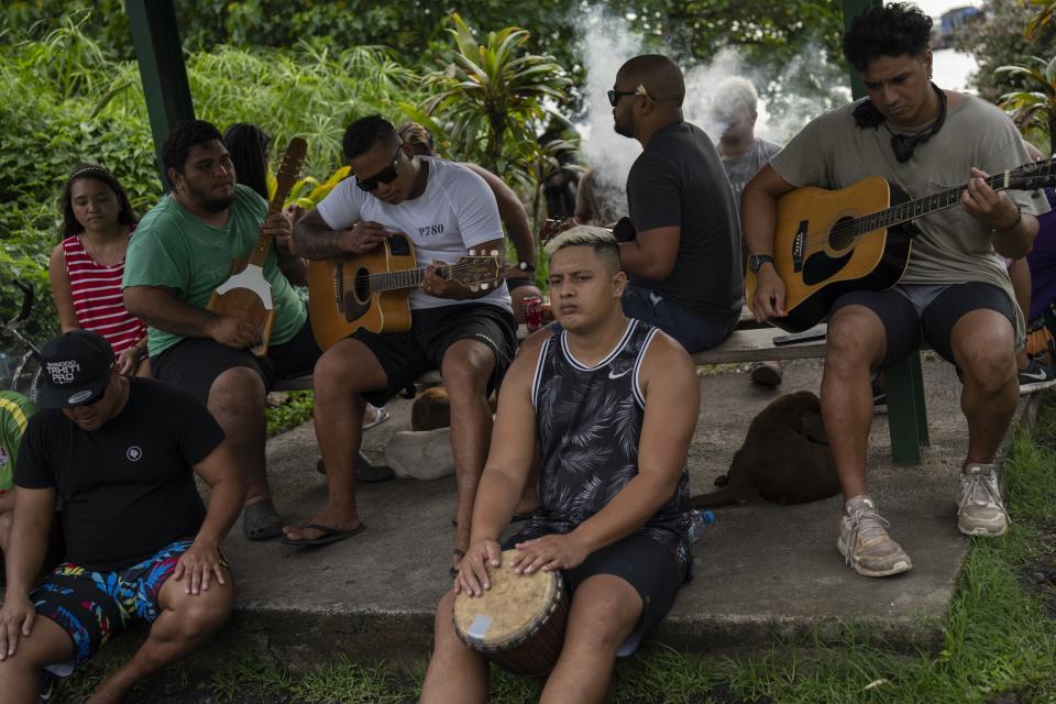A group play music together by the side of the road in Teahupo'o, Tahiti, French Polynesia, Tuesday, Jan. 16, 2024. The decision to host part of the Olympic Games here has thrust unprecedented challenges onto a small community that has long cherished and strives to protect its way of life. (AP Photo/Daniel Cole)
