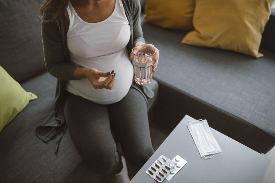 Pregnant woman sitting on sofa at home and drinking pills.