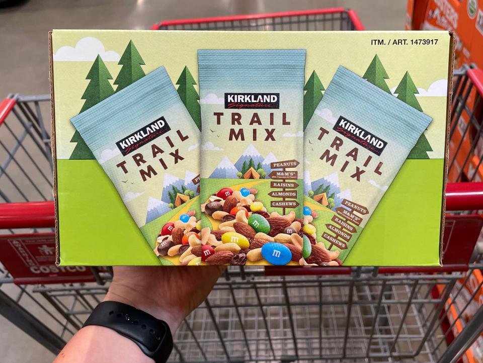 hand holding box of kirkland trail mix over cart at costco