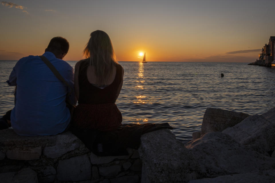 A couple enjoy the sunset on the seafront in the Adriatic town of Rovinj, Croatia, Friday, Aug. 27, 2021. Summer tourism has exceeded even the most optimistic expectations in Croatia this year. Beaches along the country's Adriatic Sea coastline are swarming with people. Guided tours are fully booked, restaurants are packed and sailboats were chartered well in advance. (AP Photo/Darko Bandic)