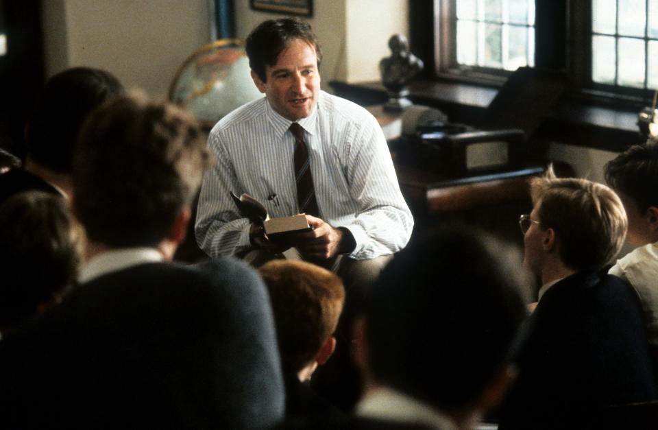 Robin reads from a book while looking at a classroom of students on the film's set
