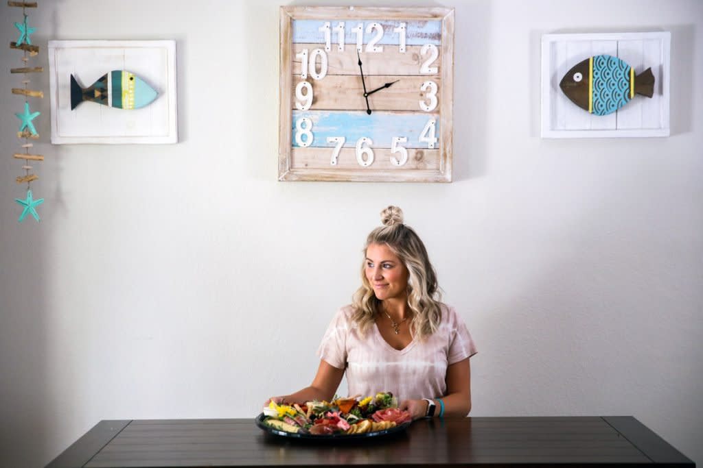 A woman sits at a table with her charcuterie board next to her. 