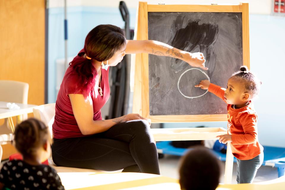 Rachel Smith, a daycare teacher, has Phallon point out the shape on a chalkboard during daycare for eighteen-month to two-year-olds on Wednesday, Jan. 26, 2022, at Nanny's Multi Level Learning Center in the Cincinnati neighborhood of Avondale. The child care industry has been dealing with staff shortages due to the COVID-19 pandemic.