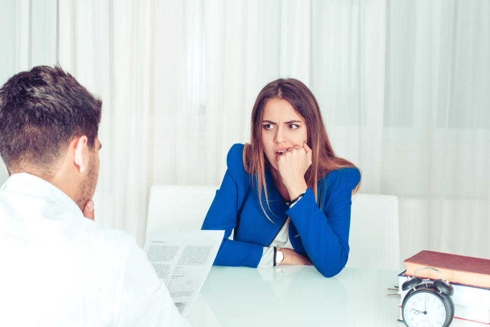 Young nervous woman watching adult man reading paper document of resume at table in office. Anonymous man reading paperwork cv, contract female candidate for vacancy biting fist in stress and worries.