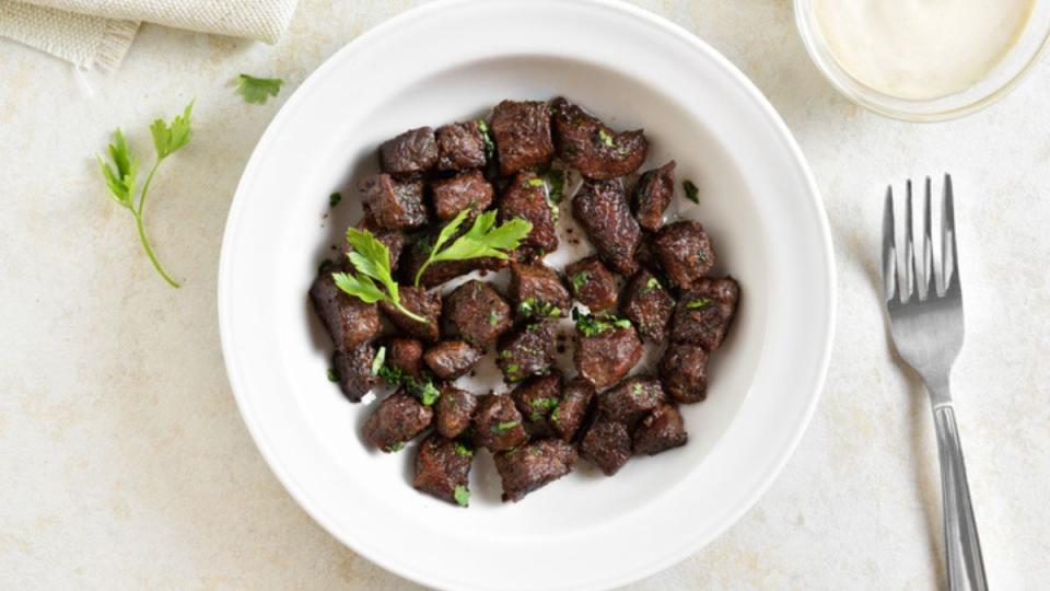 air fryer steak bites in white bowl with herbs