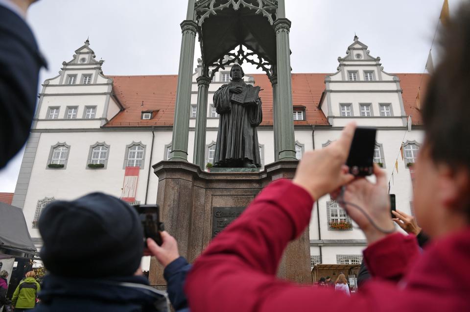 People take pictures of a statue of German Church reformer Martin Luther holding a book including his translation into German of the New Testament of the Bible at the main square in front of the city hall in Wittenberg, eastern Germany, where celebrations take place on the occasion of the 500th anniversary of the Reformation on October 31, 2017.&nbsp; (Photo: HENDRIK SCHMIDT via Getty Images)