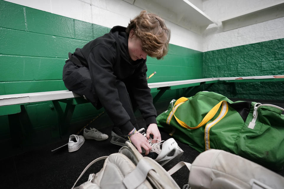 Evan Smolik ties his skates before a hockey practice Wednesday, Nov. 29, 2023, in Edina, Minn. When Evan was 14, a teammate's skate struck his neck and his jugular vein, but the neck guard he was wearing prevented the skate from cutting his carotid artery and helped save his life. (AP Photo/Abbie Parr)