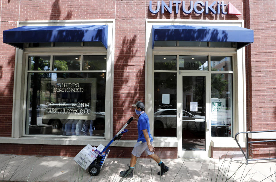 A delivery driver pushes a cart past an Untuckit men's clothes store in Dallas, Tuesday, July 7, 2020. Some big corporate names are on the government's list of 650,000 recipients of coronavirus relief loans despite the controversy that prompted other high-profile businesses to return billions of dollars in loan. Untuckit, which has 85 shirt stores, received a loan between $5 million and $10 million; the company said it used the money to keep paying its workers. (AP Photo/LM Otero)