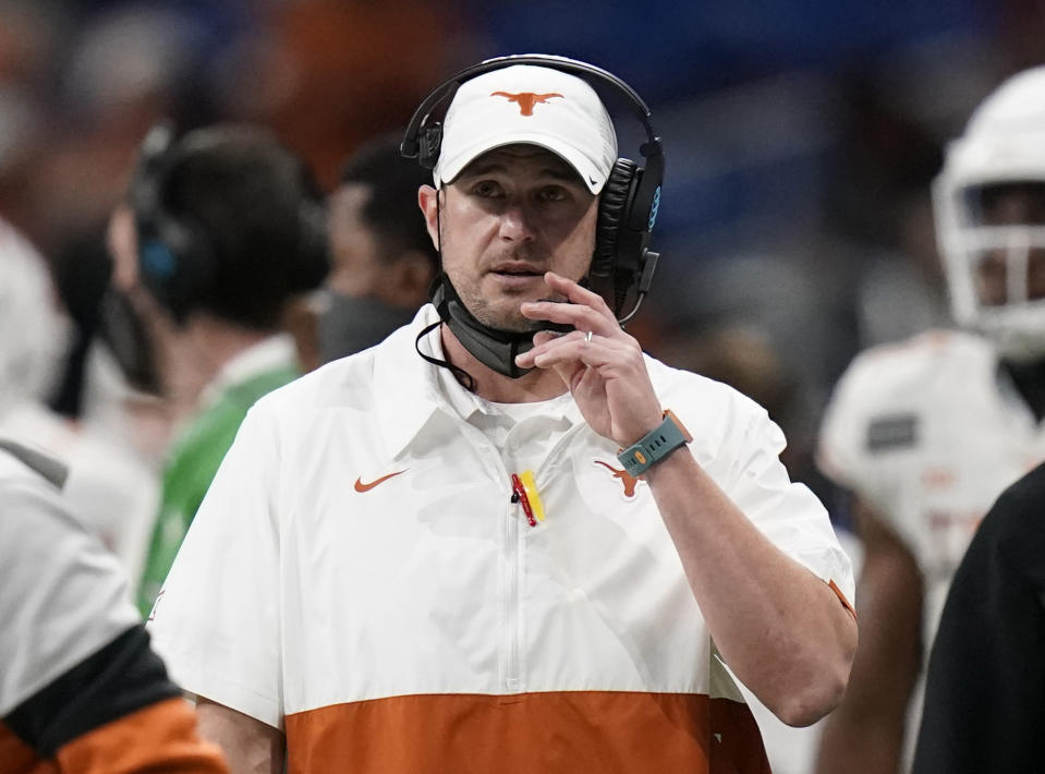 Tom Herman wears a Texas pullover shirt and hat with a headset on the sideline of a game.