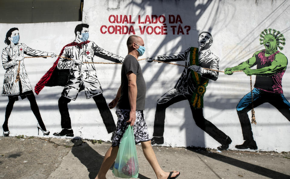 A man, wearing a protective face mask as a measure to curb the spread of the new coronavirus, walks past a mural depicting a tug-of-war between health workers and Brazil's President Jair Bolsonaro aided by a cartoon-styled coronavirus character, with a message that reads in Portuguese: "Which side are you on?," in Sao Paulo, Brazil, Friday, June 19, 2020. (AP Photo/Andre Penner)