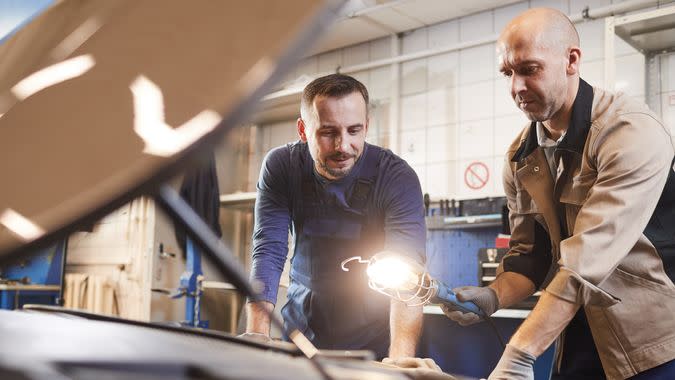 Waist up portrait of two car mechanics looking under hood of car in auto repair workshop, copy space.