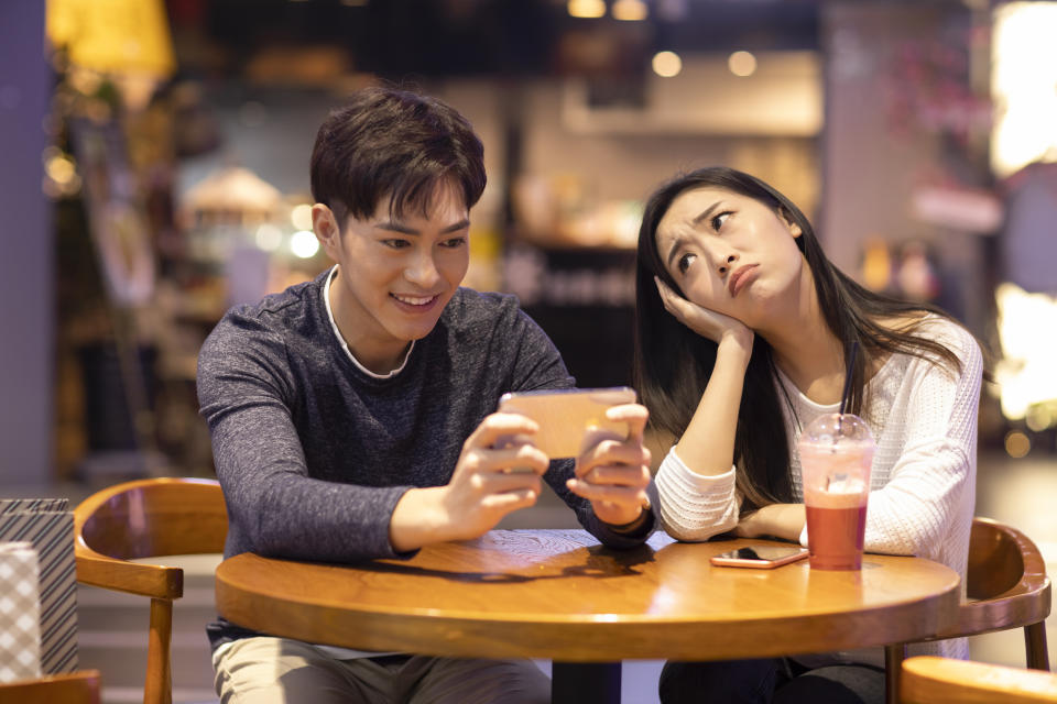 Girlfriend looks annoyed while her boyfriend uses his mobile phone.