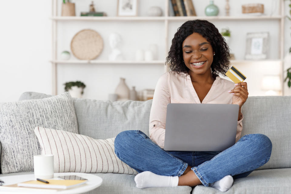 Online Shopping. Positive Young Black Girl Using Laptop and Credit Card At Home, Making Purchases In Internet, Sitting On Couch In Living Room