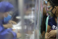 A woman wearing a mask and a face shield to prevent the spread of coronavirus watches from behind plastic sheets as teachers in protective suits demonstrate a student's electronic tablet while they prepare for online classes during the opening of school next week at the Dona Rosario High School in Quezon city, Philippines, Thursday, Oct. 1, 2020. Public schools will hold online classes using electronic gadgets and educational materials provided to students as the opening got delayed due to the coronavirus pandemic. (AP Photo/Aaron Favila)