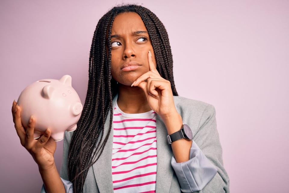 A person holding a piggy bank with a thinking or questioning expression on their face.