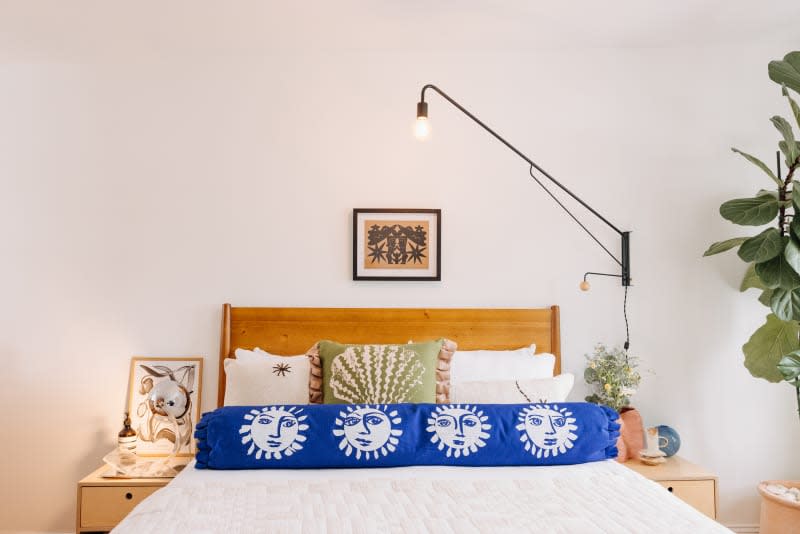 Philadelphia residence with white walls, lots of wood details: bed with wood headboard, white linens, blue and green pillows. Fiddle leaf fig to the right