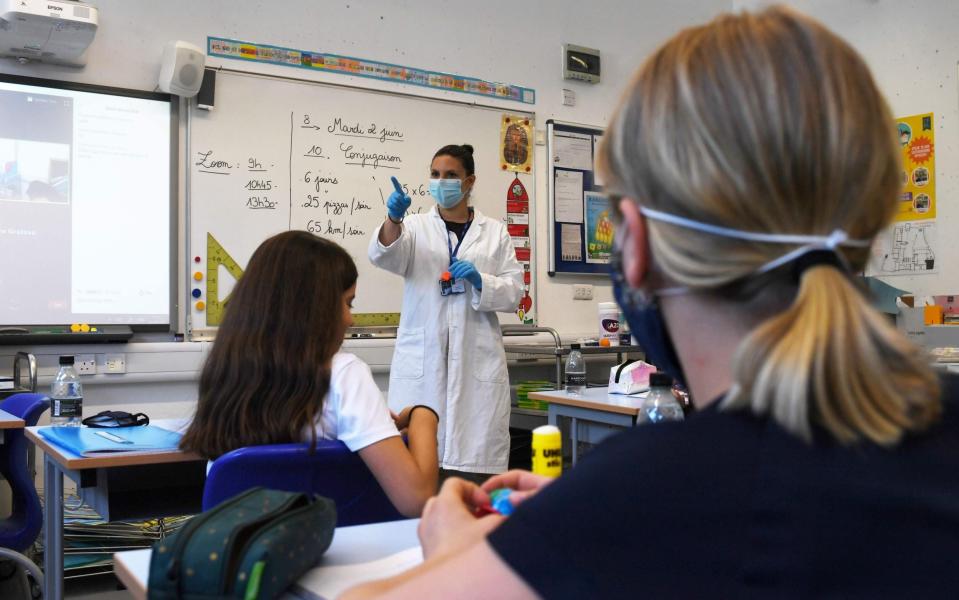 A teacher wearing a face mask teaches pupils, one also in a mask, at a school in London last month - AFP