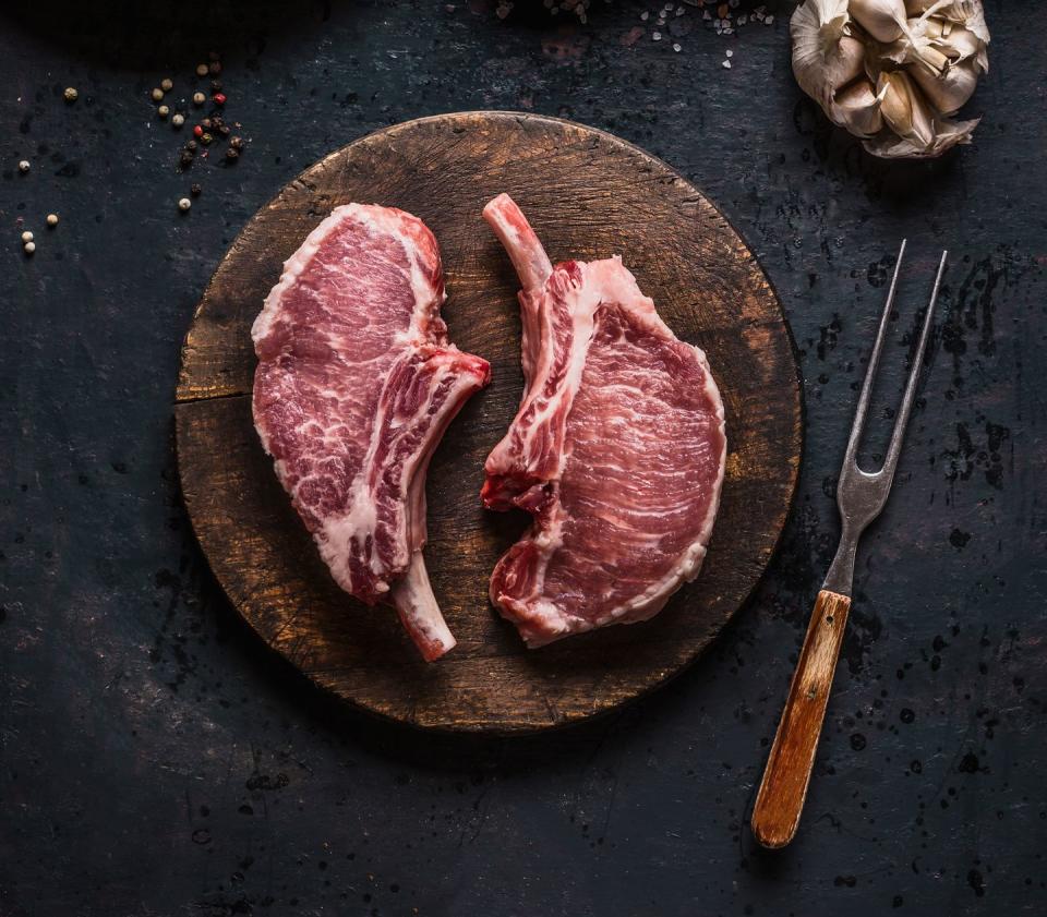 Marbled raw pork chops of Porco Iberico meat on round cutting board with meat knife. French Racks