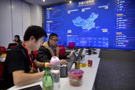 FILE - In this Nov. 11, 2018, file photo, workers use their laptops near a display showing sales data at the command center at the headquarters of an e-commerce retailer in Beijing. Remarks by the head of Chinese online business giant Alibaba that young people should work 12-hour days, six days a week if they want financial success have prompted a public debate over work-life balance in the country. (AP Photo/Mark Schiefelbein, File)