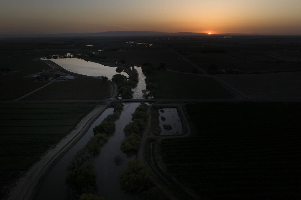 Twilight settles in over the North Fork Kings River in the Island District of Lemoore, Calif., as the sun sets over the horizon Wednesday, April 19, 2023. The tree-lined Island District is bracing for the massive amounts of snow in the Sierra Nevada to melt into so much water this spring that it simply can't all flow into the north fork of the Kings River, which runs toward the Pacific Ocean. (AP Photo/Jae C. Hong)