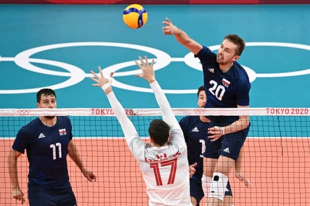 Poland's Mateusz Bieniek, right, hits the ball past Canadian Graham Vigrass, centre left, in the men's preliminary round pool A volleyball match that resulted in Poland winning 3-0 (25-15, 25-21, 25-16) over Canada on Sunday in Tokyo. (Anne-Christine Poujoulat/AFP via Getty Images - image credit)