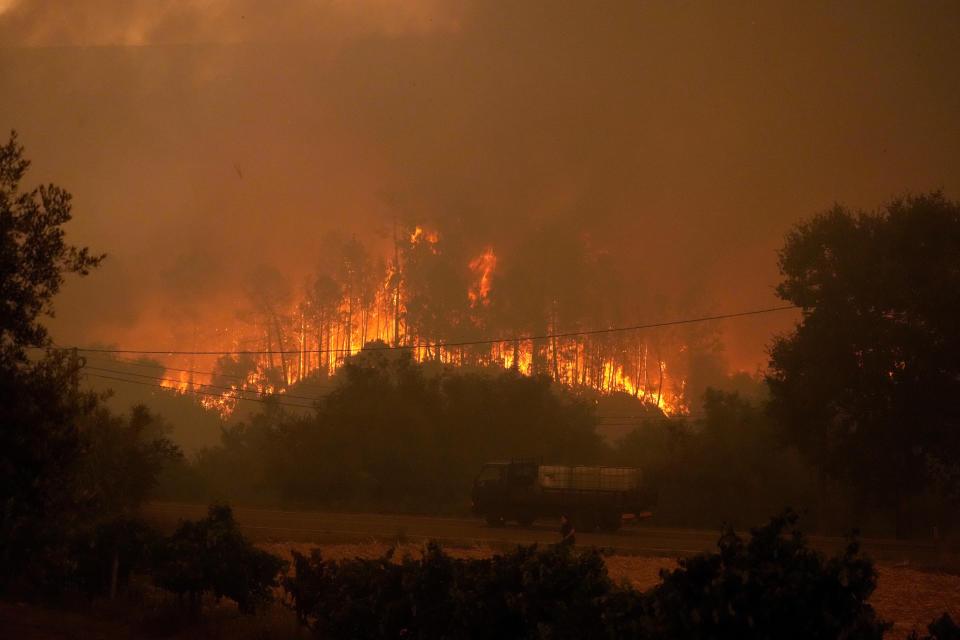 A truck carrying tanks with water drives by a forest fire as smoke darkens the sky in the village of Bemposta, near Ansiao, central Portugal, Wednesday, July 13, 2022. Thousands of firefighters in Portugal continue to battle fires all over the country that forced the evacuation of dozens of people from their homes. (AP Photo/Armando Franca)