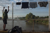 Un migrante hondureño observa el río Suchiate, que separa a México, derecha, y a Guatemala, izquierda, desde un puente en donde secan ropa en Tecún Umán, Guatemala, al amanecer el domingo 21 de octubre de 2018. (AP Foto/Oliver de Ros)