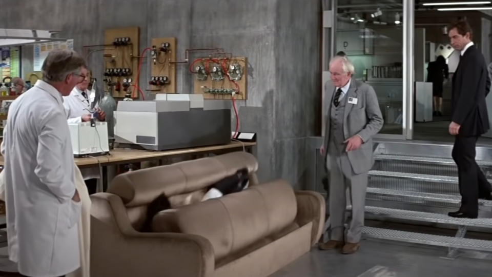 Desmond Llewelyn and Timothy Dalton watch the revolving couch at work, in The Living Daylights.