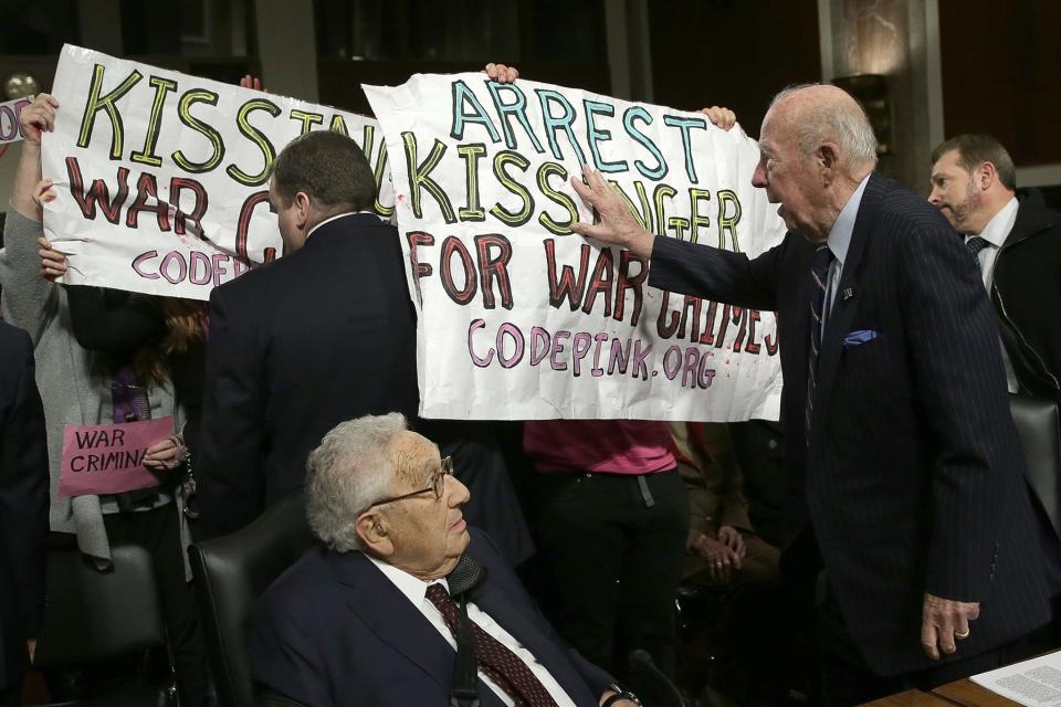 Former US Secretary of State George Shultz (C) pushes away protesters shouting 