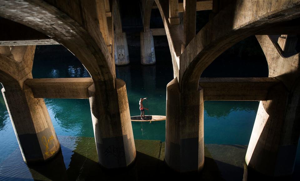 Tony Smith, the owner of Jarvis Boards, paddles beneath the Baton Springs Road bridge on Barton Creek in Austin in 2017. Construction on the bridge could begin as soon as 2026.