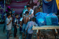 A Rohingya activist distributes new clothes among refugees at a refugee camp alongside the banks of the Yamuna River in the southeastern borders of New Delhi, sprawling Indian capital, July 1, 2021. Millions of refugees living in crowded camps are waiting for their COVID-19 vaccines. For months, the World Health Organization urged countries to prioritize immunizing refugees, placing them in the second priority group for at-risk people, alongside those with serious health conditions. (AP Photo/Altaf Qadri)