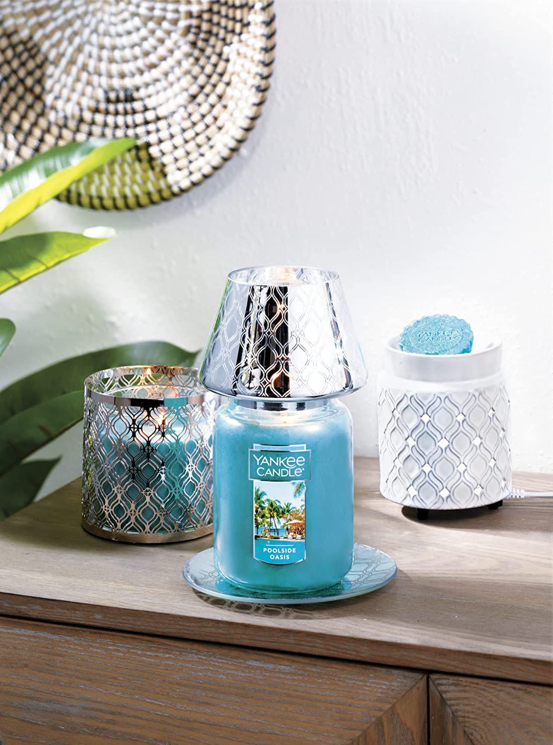 Three Yankee Candles on wooden side table next to a banana leaf plant.