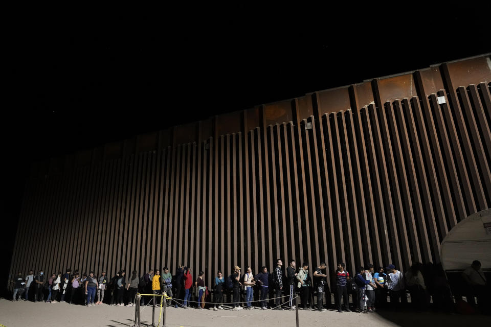 People line up against a border wall as they wait to apply for asylum after crossing the border from Mexico Tuesday, July 11, 2023, near Yuma, Arizona. Thousands of migrants from the north African country of Mauritania have arrived in the U.S. in recent months, following a new route taking them to Nicaragua and up through the southern border. (AP Photo/Gregory Bull)