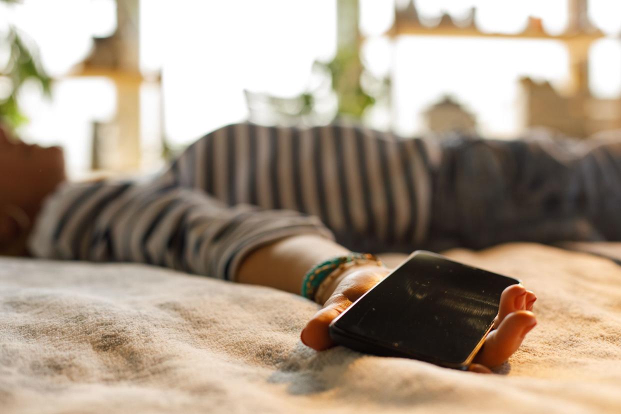 Selective focus shot of unrecognizable woman lying on back on her cozy bed, holding her smart phone and waiting for a taxi she called.