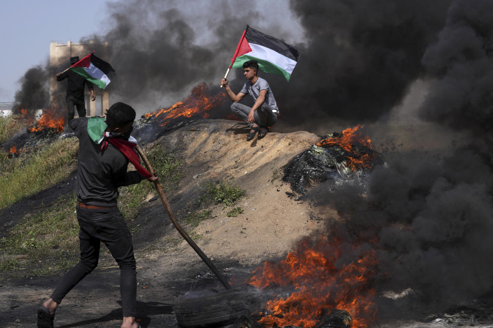 Palestinians burn tires and wave the national flag during a protest against an Israeli police raid of the Al-Aqsa Mosque compound in Jerusalem's Old City early Wednesday, along the border fence with Israel, east of Gaza City, Wednesday, April 5, 2023. (AP Photo/Adel Hana)