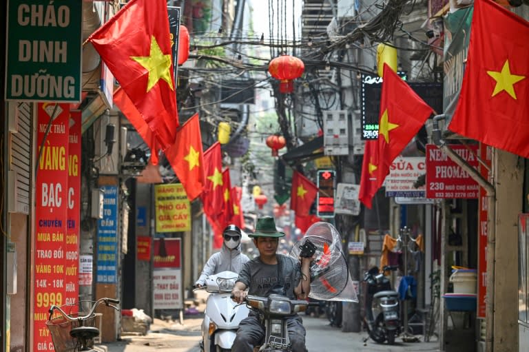 Un homme porte un ventilateur le long d'une rue bordée de drapeaux nationaux vietnamiens à Hanoï, le 30 avril 2024 (Nhac NGUYEN)