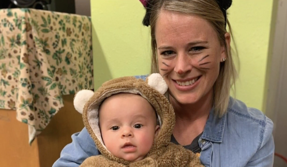 Amanda Zupancic holds a baby while she's dressed in a costume with whiskers. 