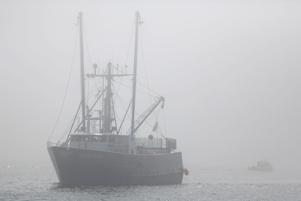 A fishing boat emerges from the fog as a small boat makes its way into it in New Bedford harbor.