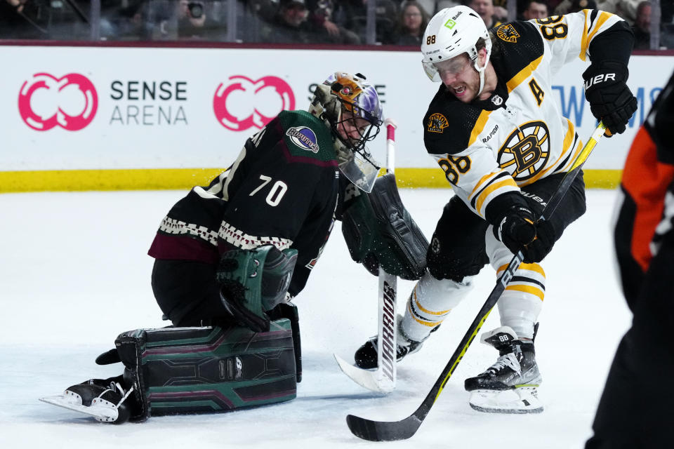 Arizona Coyotes goaltender Karel Vejmelka (70) slides over to make the save on a shot by Boston Bruins right wing David Pastrnak (88) during the second period of an NHL hockey game in Tempe, Ariz., Friday, Dec. 9, 2022. (AP Photo/Ross D. Franklin)
