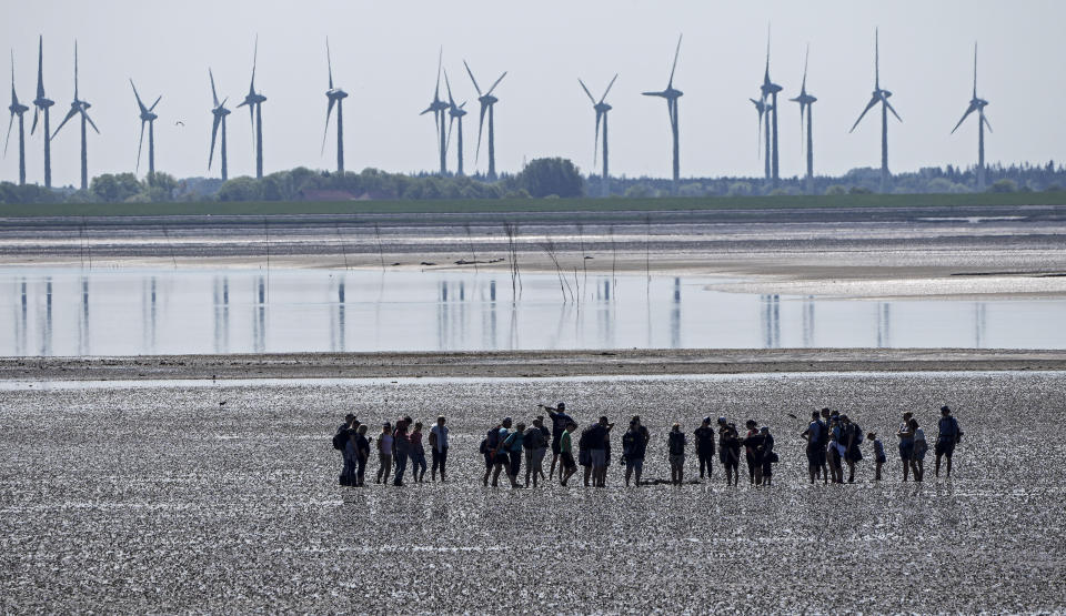 FILE - In this June 1, 2021 file photo, people explore the wadden sea at the island Norderney, Germany, in front of wind turbines, producing renewable energy. The cuts in greenhouse gas emissions pledged by governments around the world aren't enough to achieve the headline goal of the Paris climate accord, according to a United Nations report published Friday. The U.N. climate office said it reviewed all the national commitments submitted by Paris pact signatories until July 30 and found that they would result in emissions of planet-warming gas rising nearly 16% by 2030, compared with 2010 levels. (AP Photo/Martin Meissner, File)