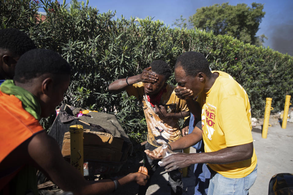 People are affected by tear gas fired by police trying to disperse a protest by factory workers demanding salary increases in Port-au-Prince, Haiti, Wednesday, Feb. 23, 2022. It is the first day of a three-day strike organized by factory workers who also shut down an industrial park earlier this month to protest pay. (AP Photo/Odelyn Joseph)