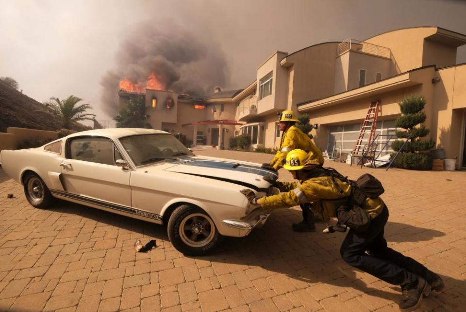 Firefighters push a car from a garage as a home burns in Malibu.